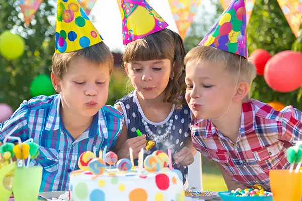 Three young children blowing out candles on a birthday cake.